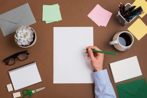 close-up-person-s-hand-writing-white-blank-paper-with-stationeries-desk_23-2147979160-4